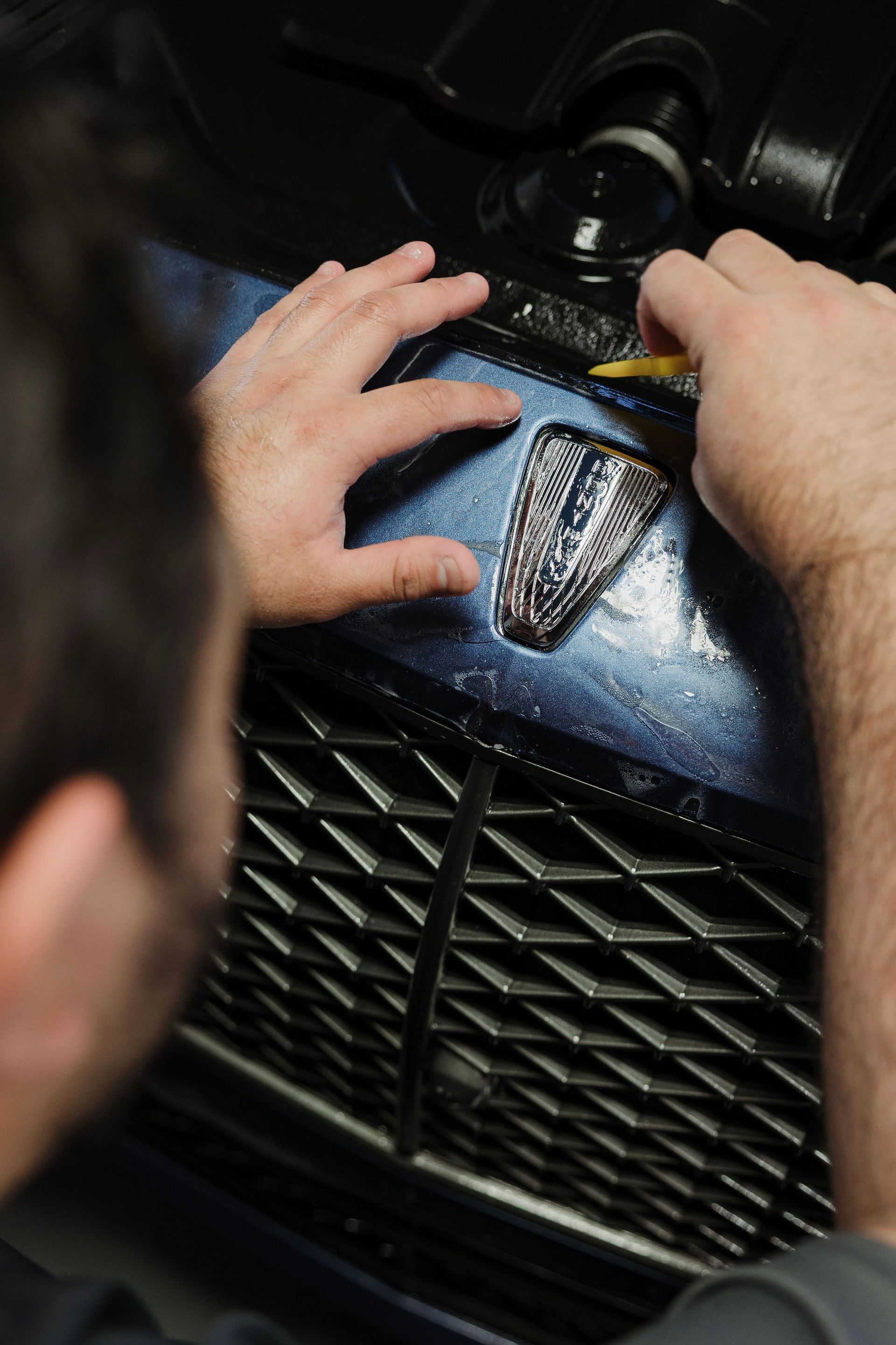 Hands adjusting a blue car grille and hood badge close-up