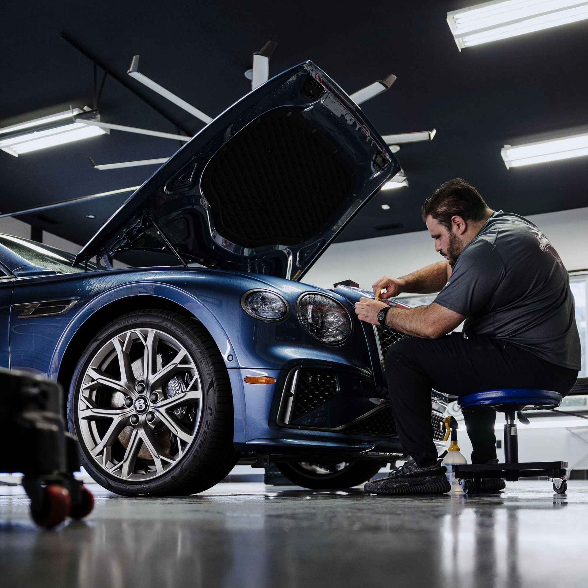 Mechanic working on a blue sports car in a garage with the hood open
