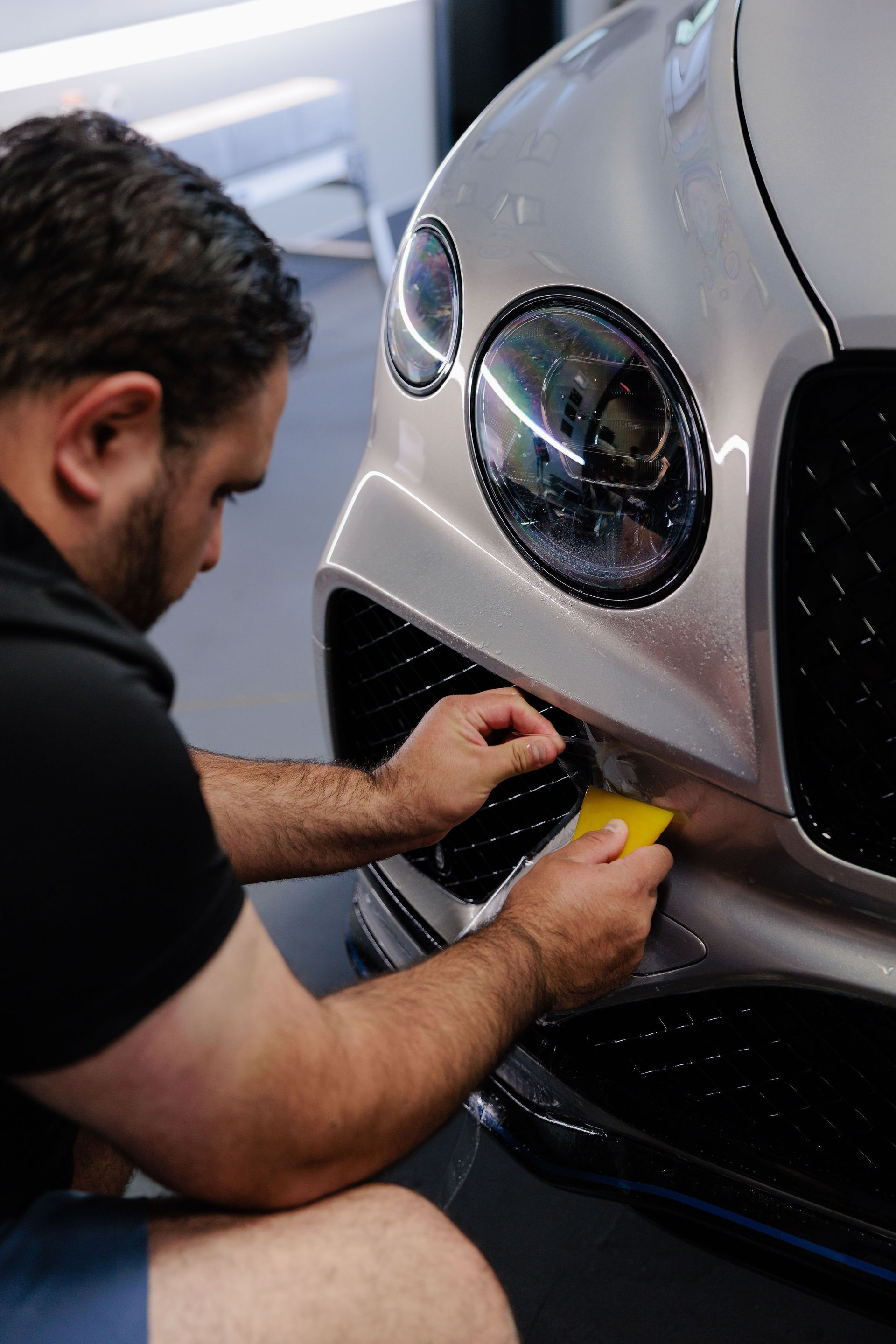 Man sprays soapy water on a black Ferrari in a car detailing shop.