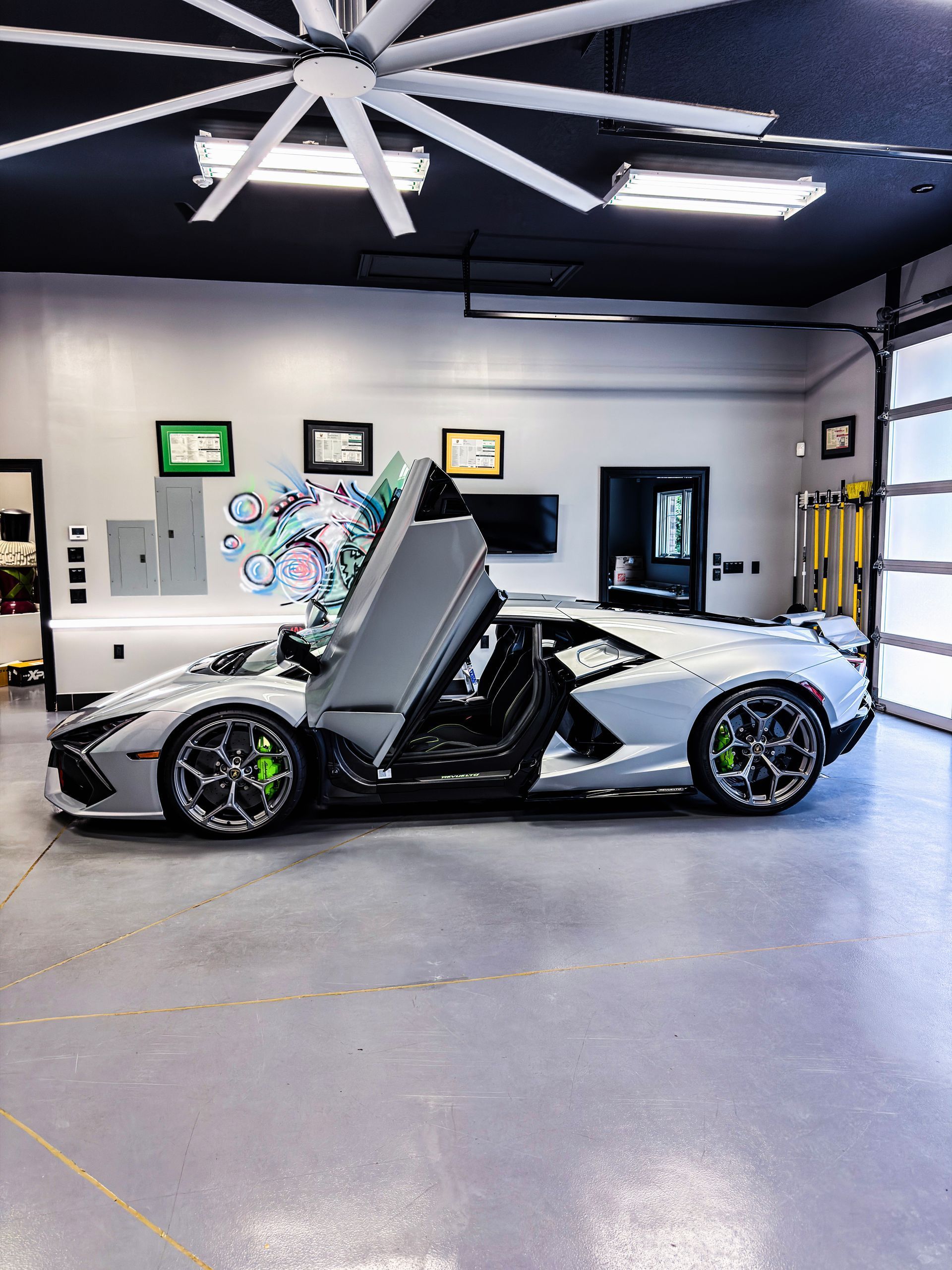 White sports car with scissor doors open in a modern garage, showing black accents and bright green brake calipers