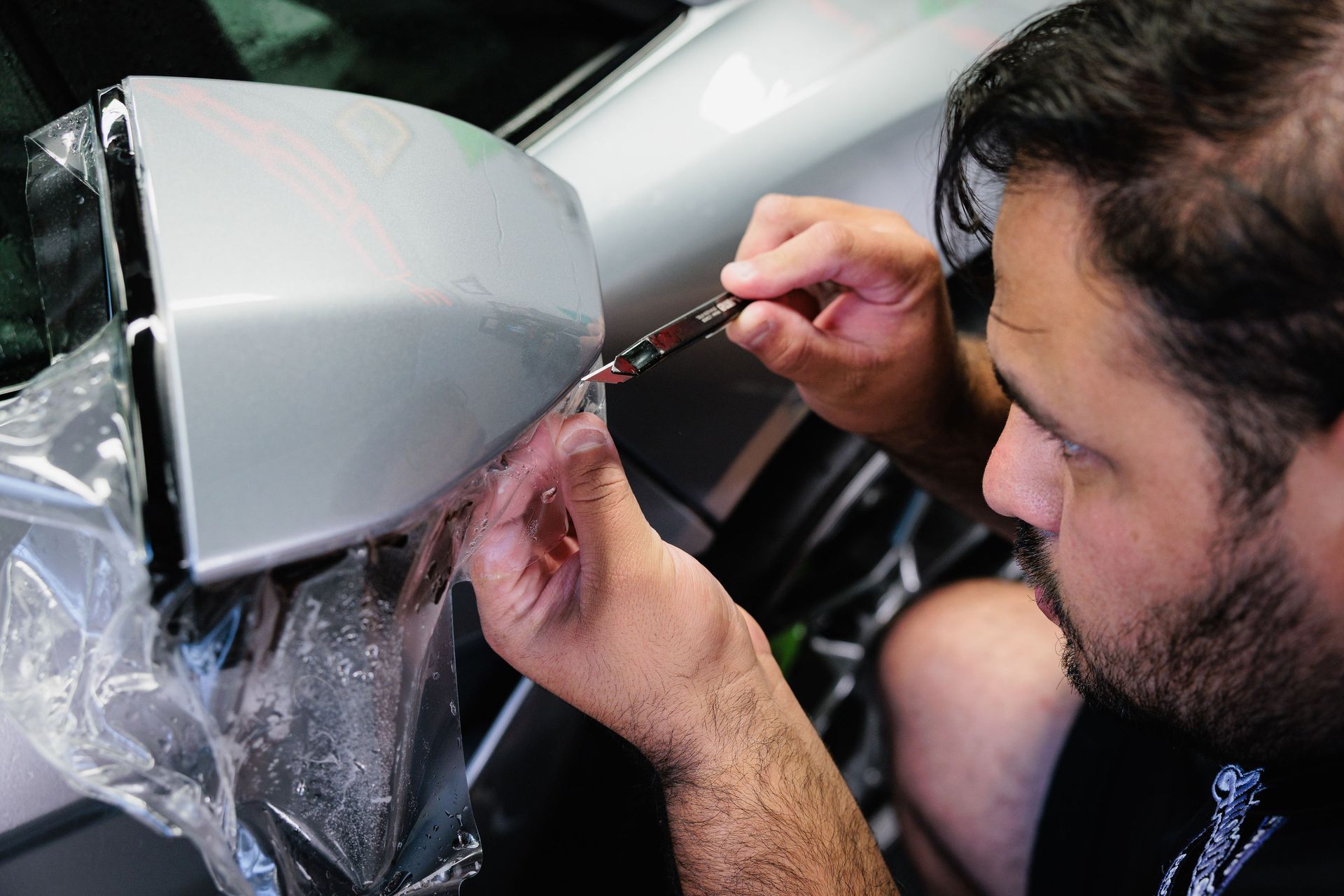 Person applying clear film to a silver car panel with a small brush