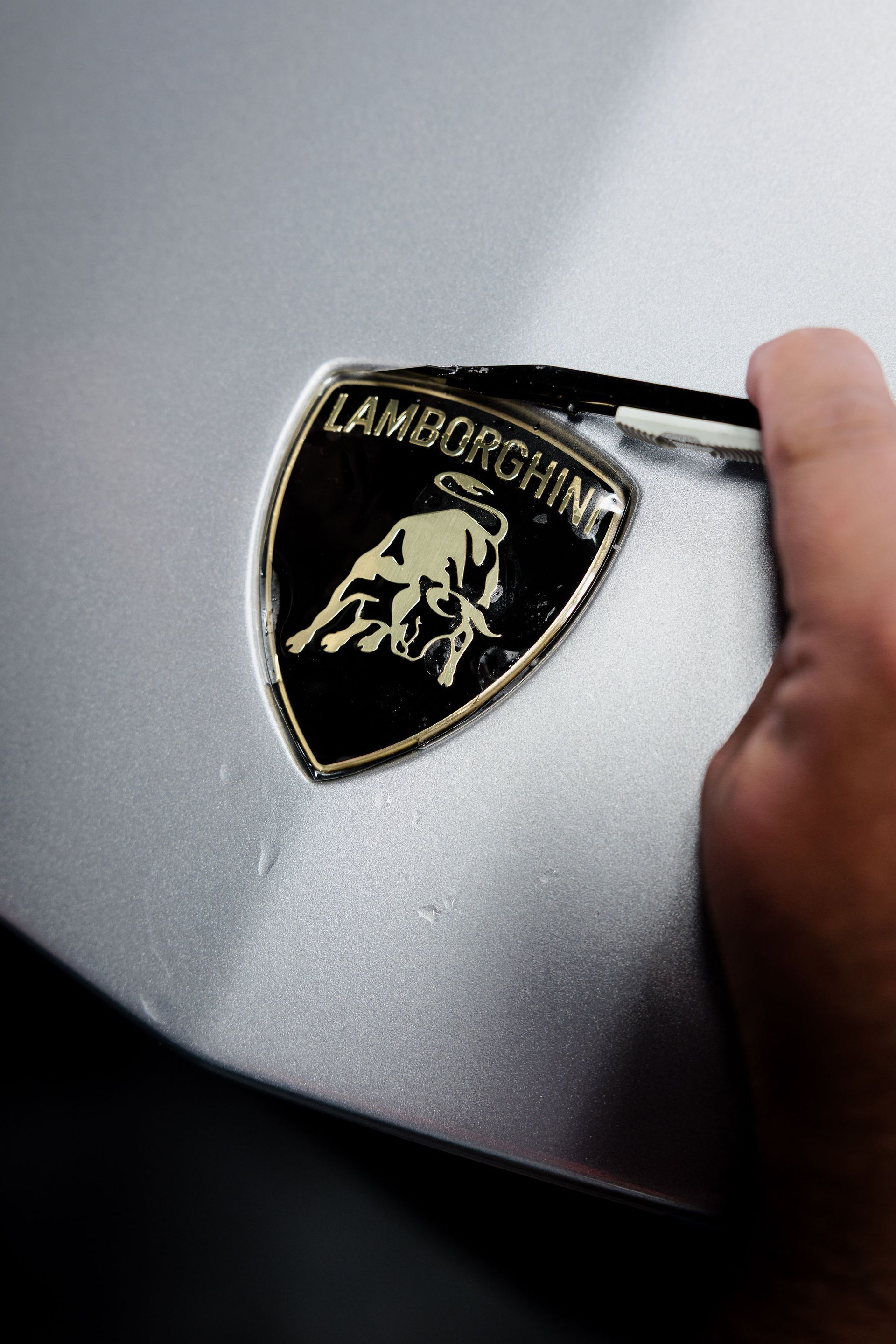 Hand placing a Lamborghini emblem on a silver car hood