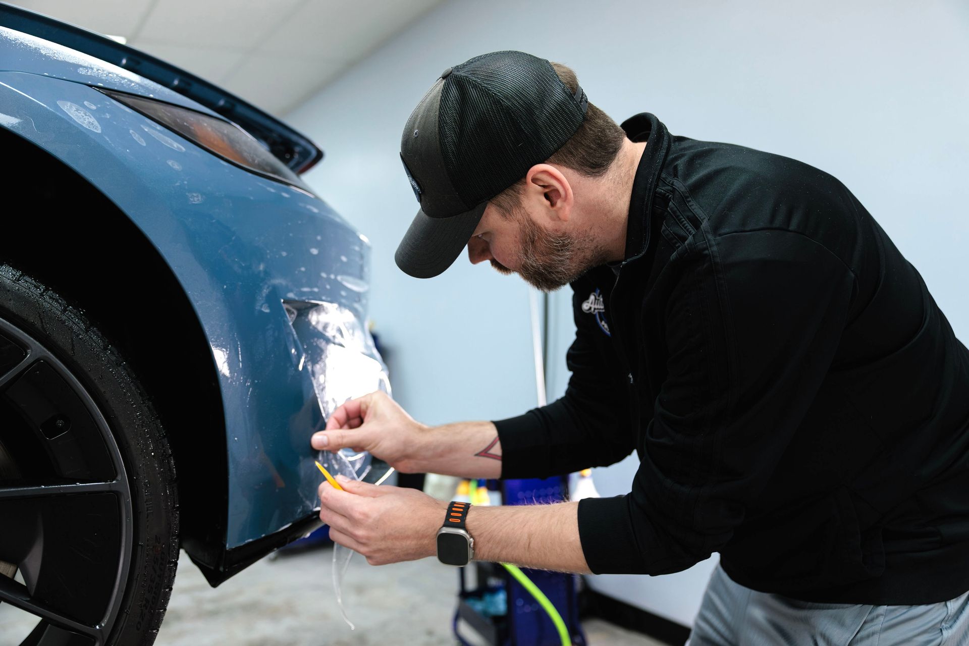 Detailing technician polishing the front bumper of a blue car in a garage