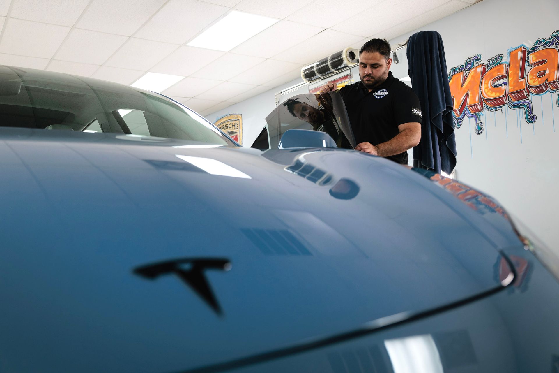 Blue Tesla in a garage while a man wipes or cleans the windshield nearby