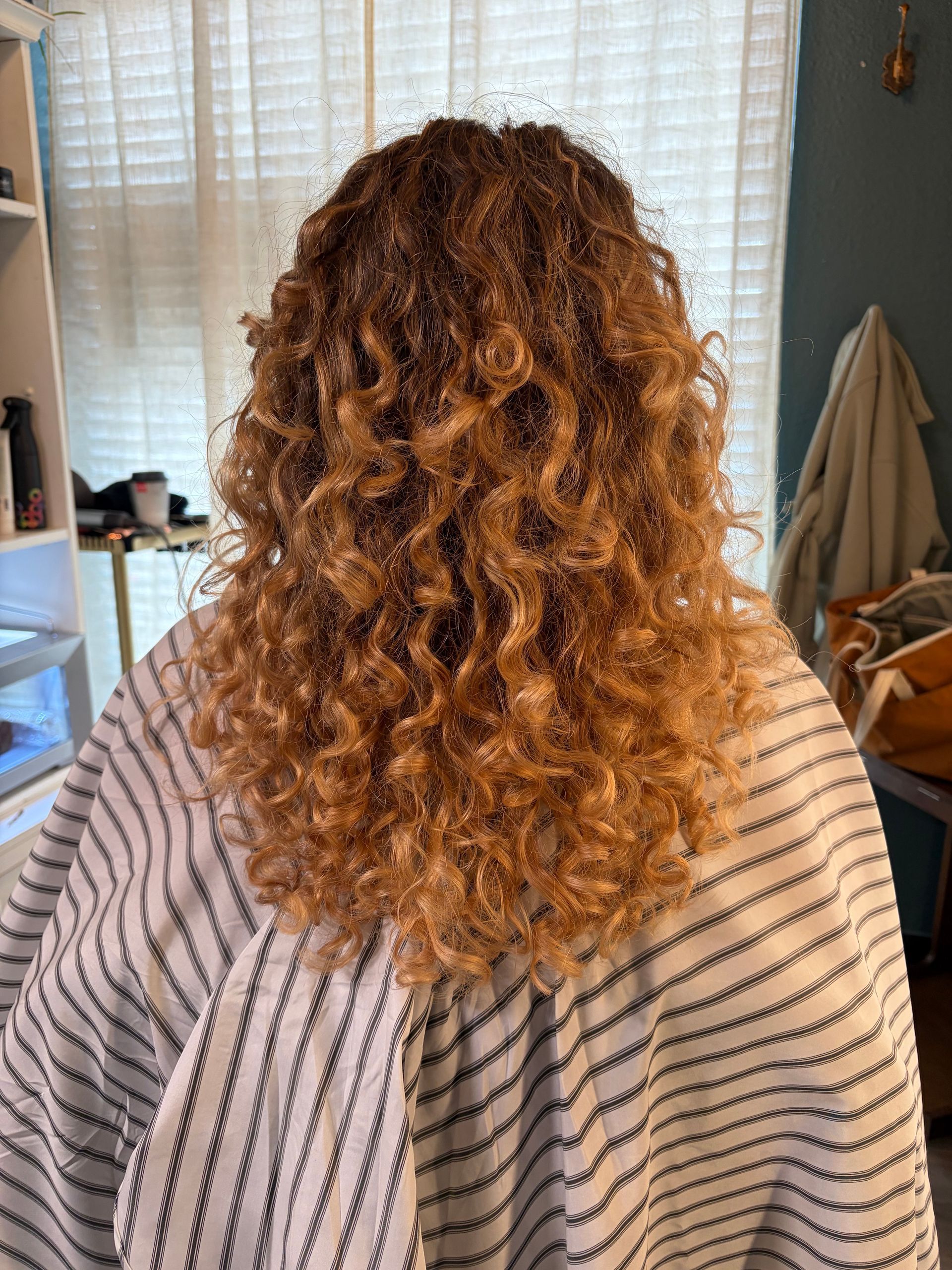 Back view of curly, highlighted blonde hair at shoulder length, styled in a salon setting.