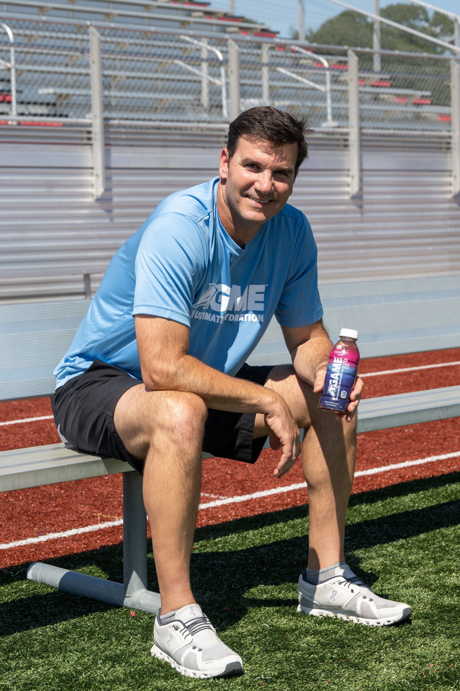 A man is sitting on a bench on a track holding a bottle of water.