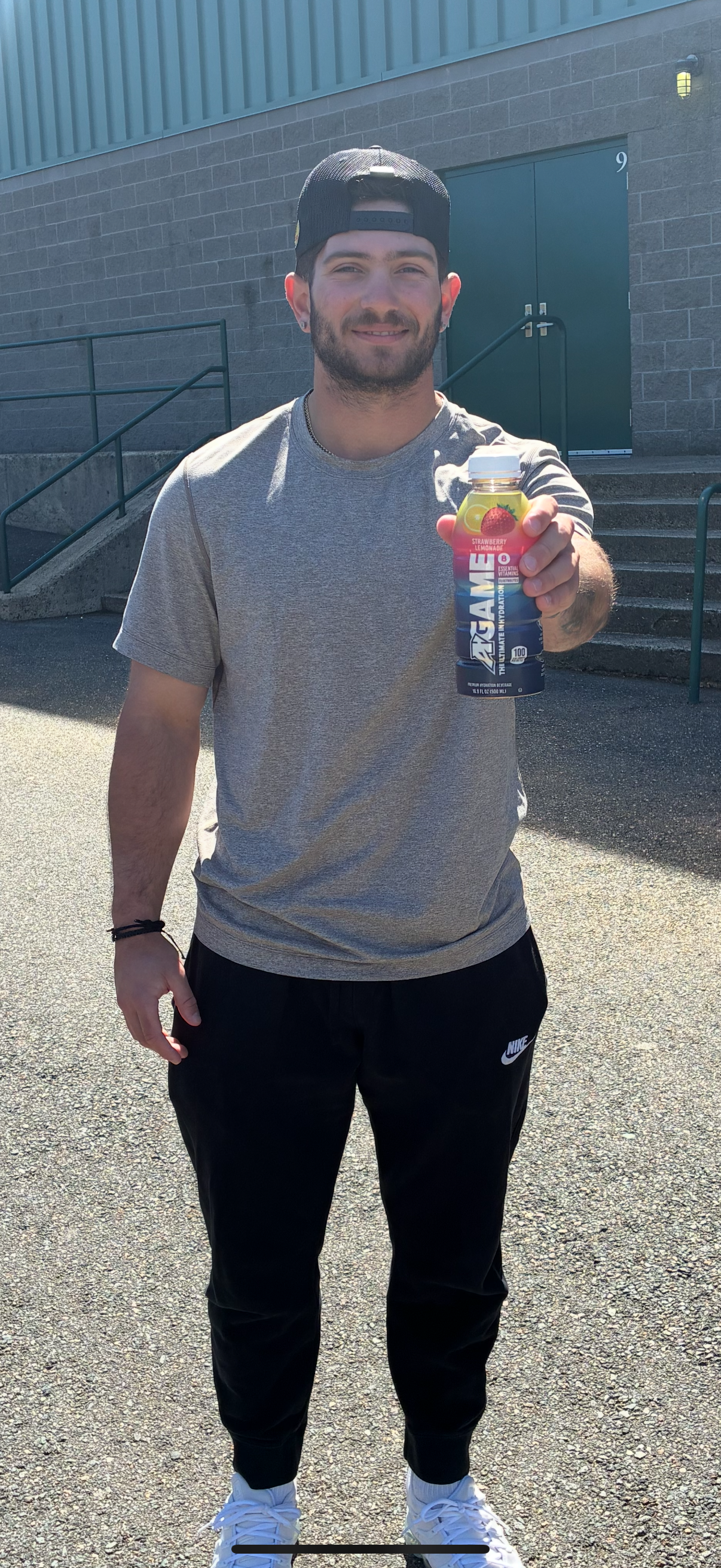 A man is standing in front of a building holding a can of energy drink.