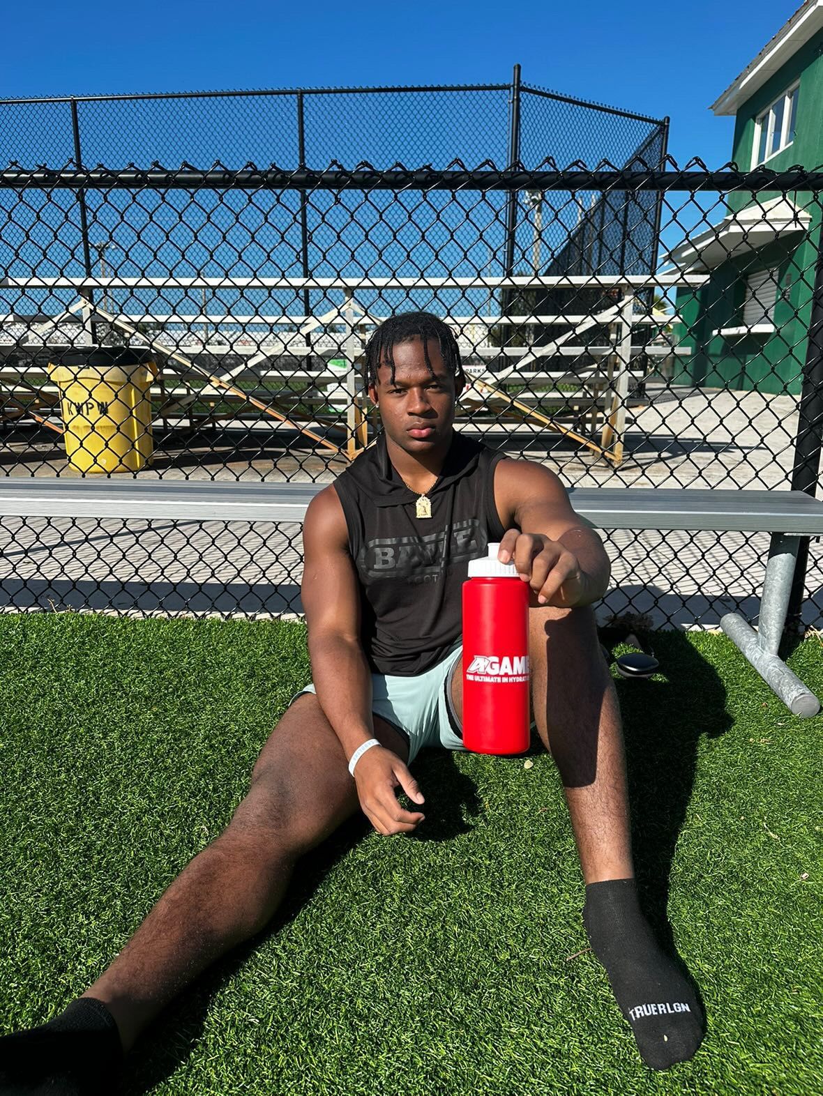 A man is sitting on the grass holding a red water bottle.