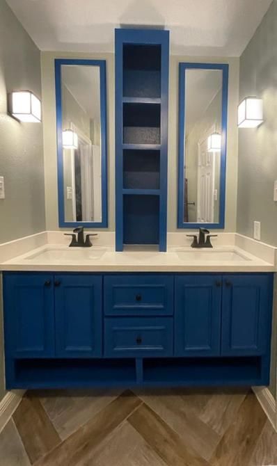 A bathroom with two sinks , two mirrors , and blue cabinets.