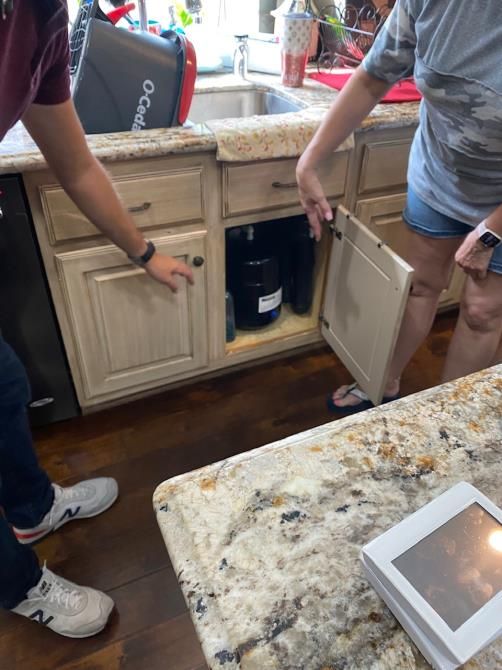 A man and a woman are looking under a sink in a kitchen.