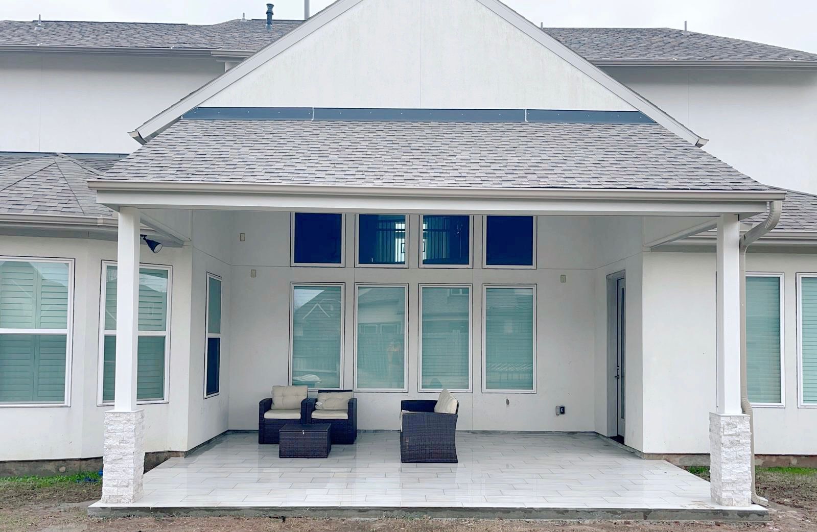 A white house with a covered patio with chairs and a table.