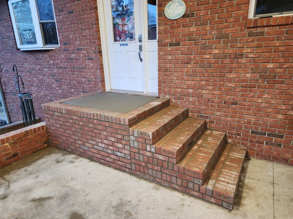 Brick front porch with white door and short steps leading to a concrete walkway.