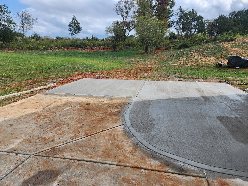 Concrete slab and curved paved area at a construction site beside grassy land and trees
