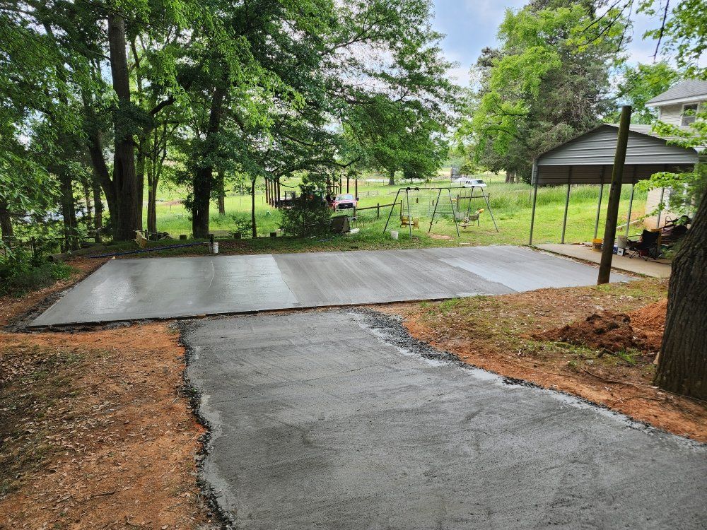 Freshly poured concrete driveway leading to a covered carport in a wooded yard