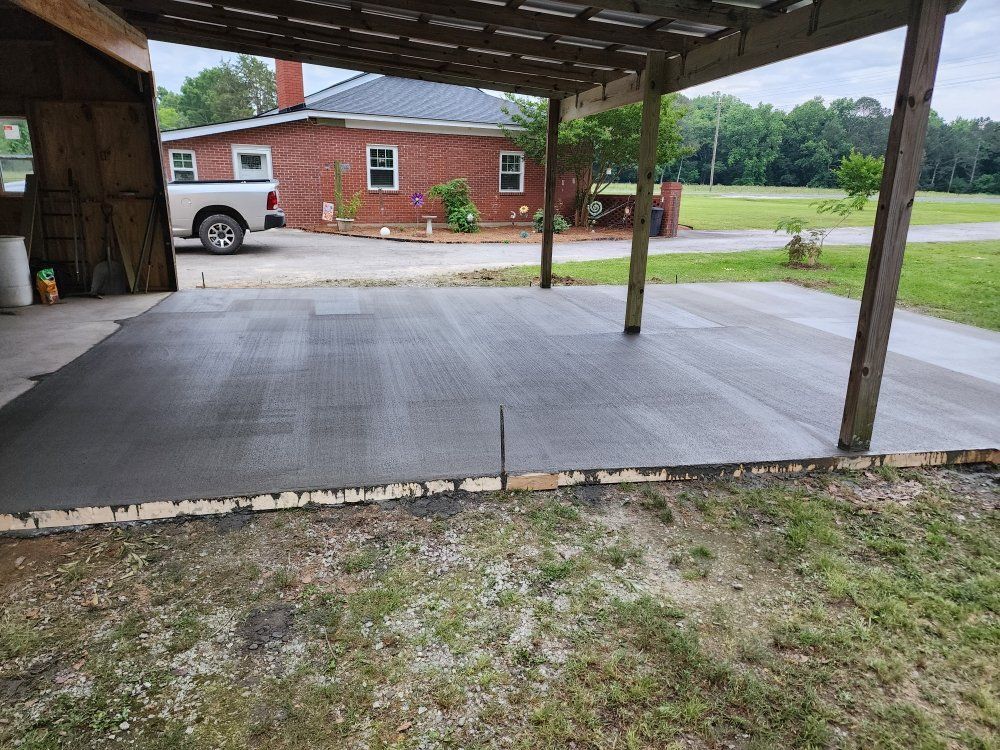 Concrete slab under a carport beside a red brick building and grassy yard