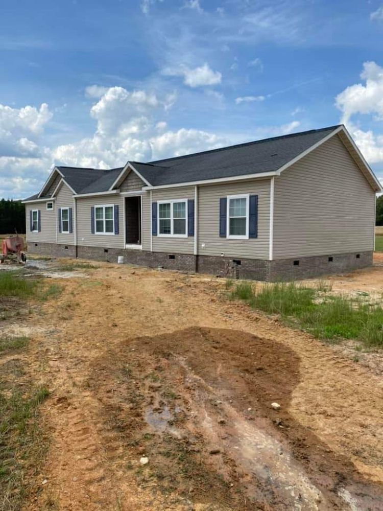 New beige single-story house under construction with dirt yard and blue sky