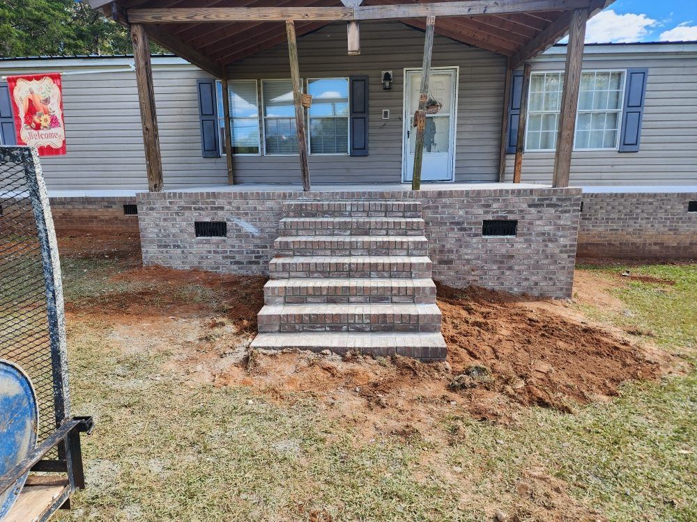 Front porch with concrete steps leading to a mobile home entrance, with unfinished dirt landscaping in front.