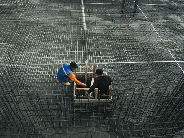 Two workers arranging rebar in a concrete foundation area.