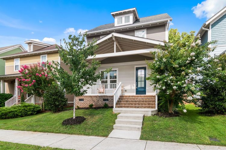 Single-family house with front porch, manicured lawn, and stone steps in a suburban neighborhood
