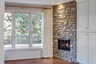 Empty room with large windows, stone fireplace, and white built-in cabinets