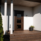 Front porch with white columns, wooden door, brick steps, and a potted plant in sunlight