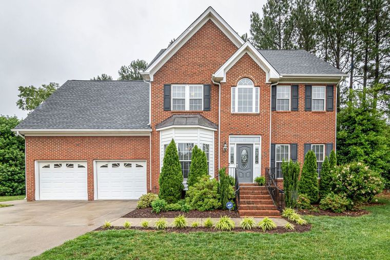 Two-story brick house with attached double garage, white trim, and landscaped front yard