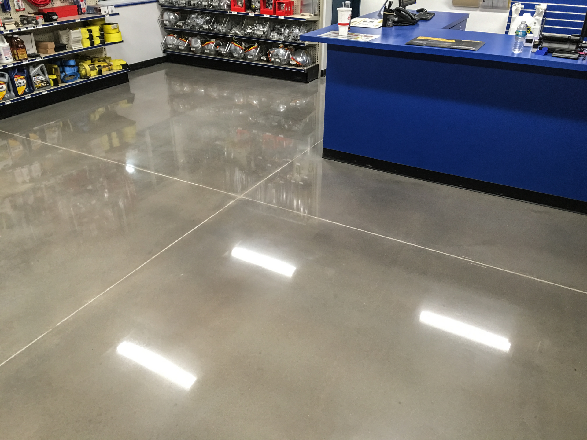 Empty store interior with glossy gray floor, shelves of products, and a blue counter on the right.