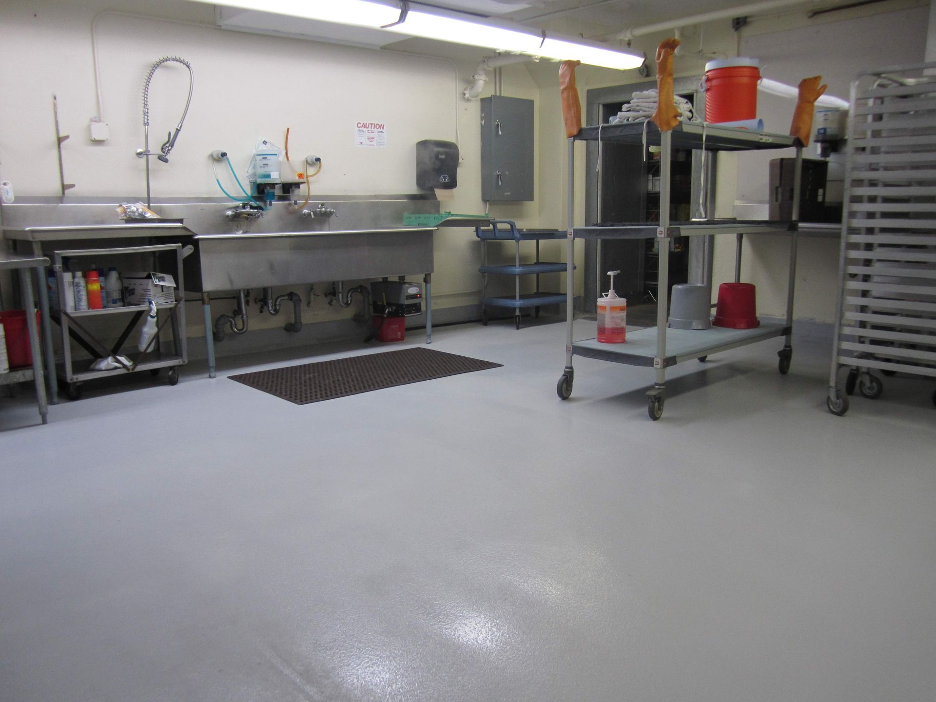 Industrial kitchen with stainless steel counters, shelves, and cleaning supplies on a glossy floor