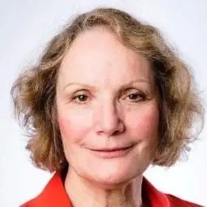 A headshot of a person with shoulder-length, wavy, light-brown hair, wearing a red top against a light-gray background.