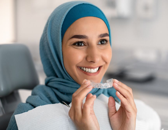 Dentist with green gloves pointing at a shade guide for a smiling patient.