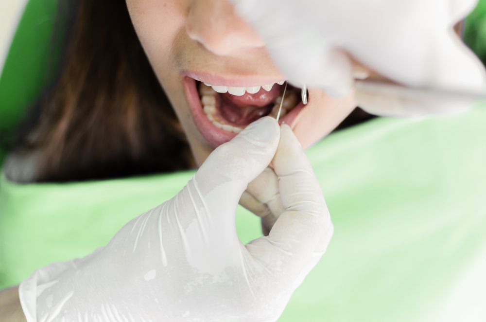 Dentist examining a person's teeth with tools in a dental office.