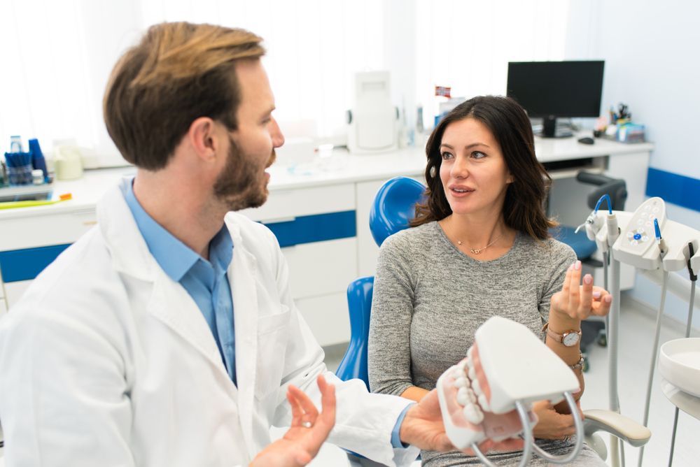 Dentist showing teeth model to patient in a bright dental office.