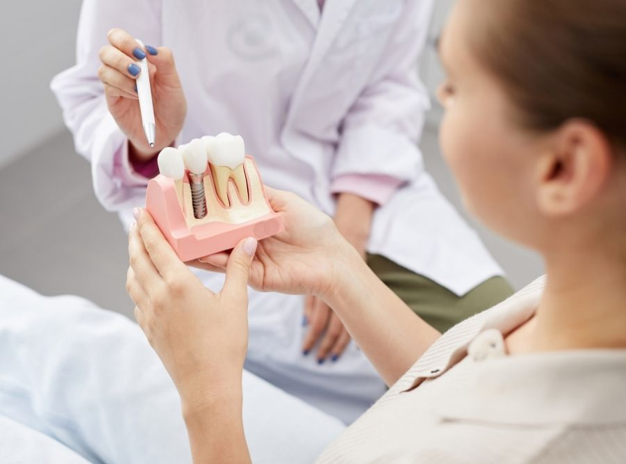 Dentist showing patient a tooth model, pointing with a tool in a dental office.