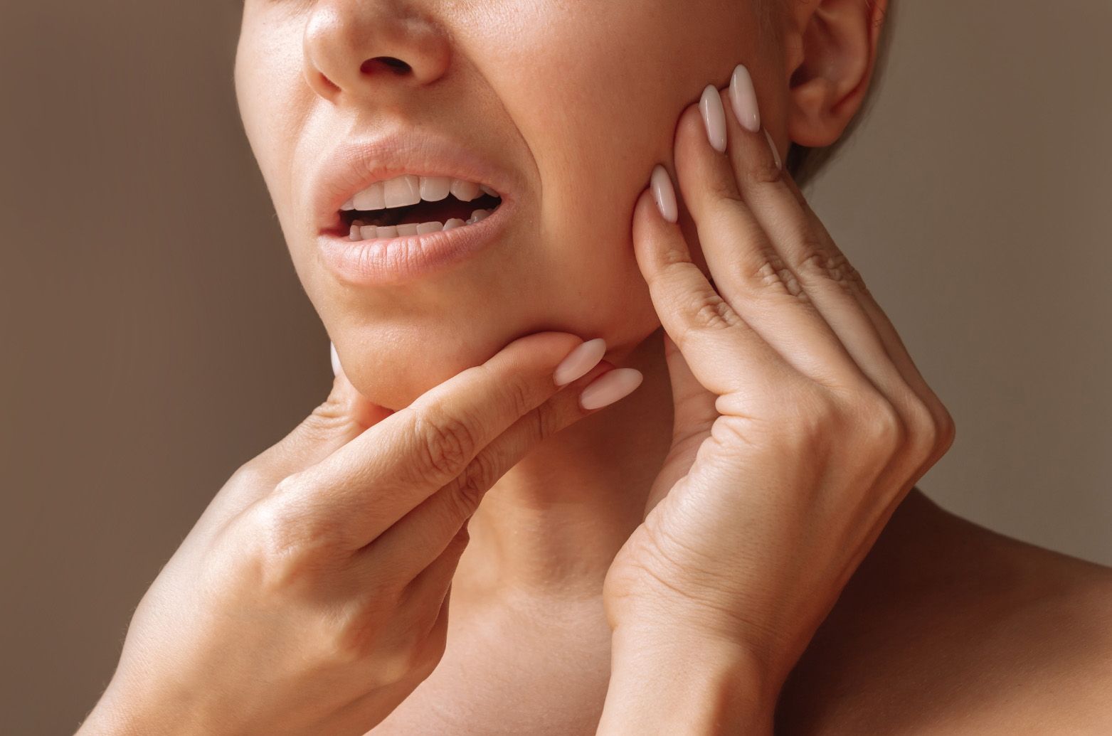 Woman with open mouth and hands on face, appears to be in pain, neutral background.