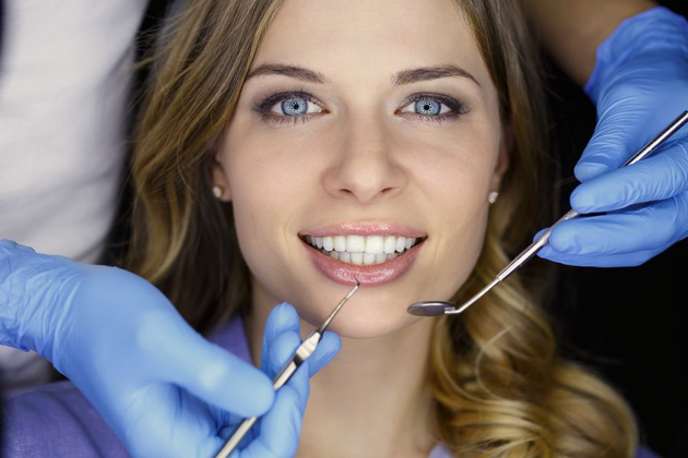 Woman at dentist, mouth open, tools in view. Blue gloves, bright smile.
