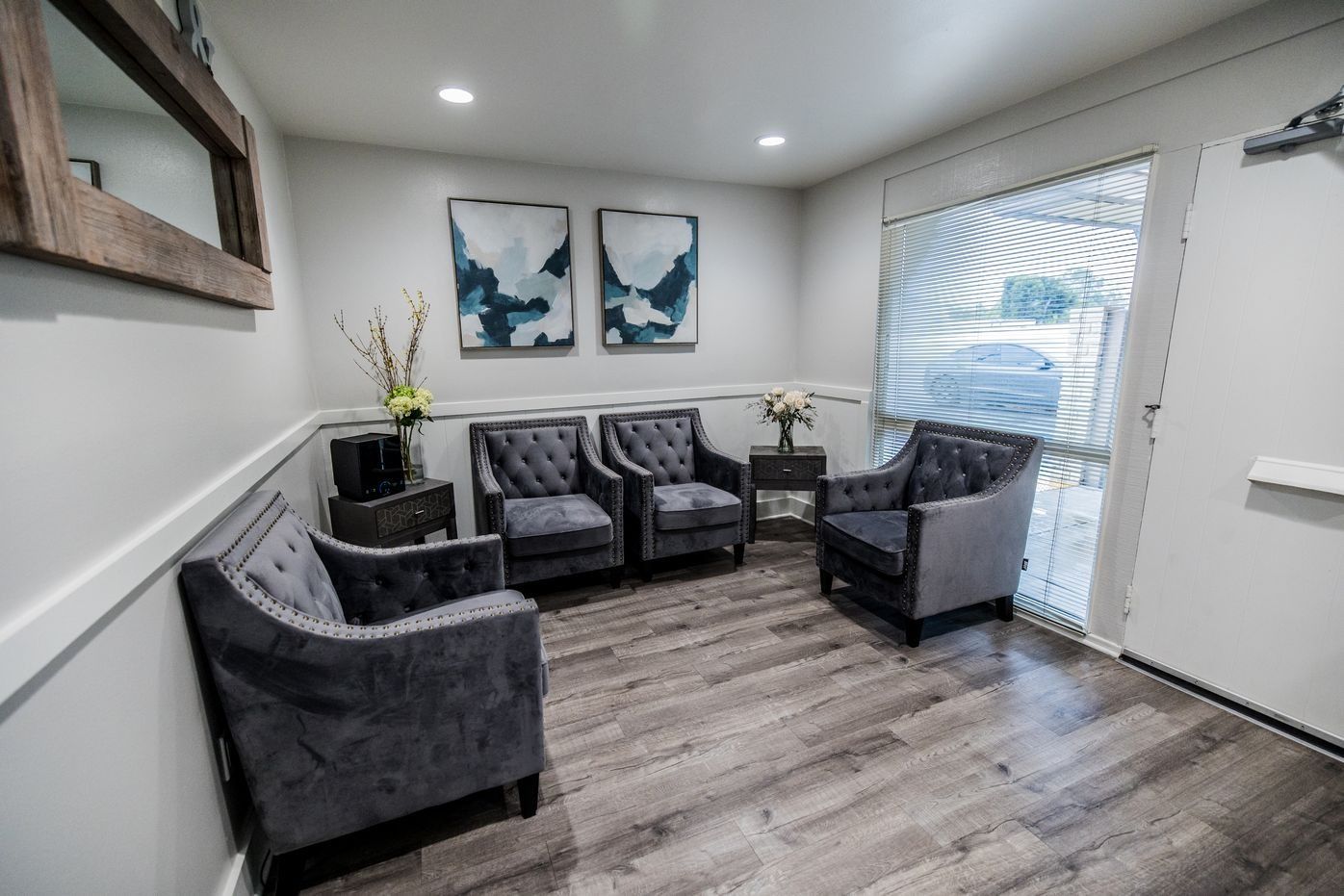 Waiting room with gray upholstered chairs, artwork, and wood-look flooring.