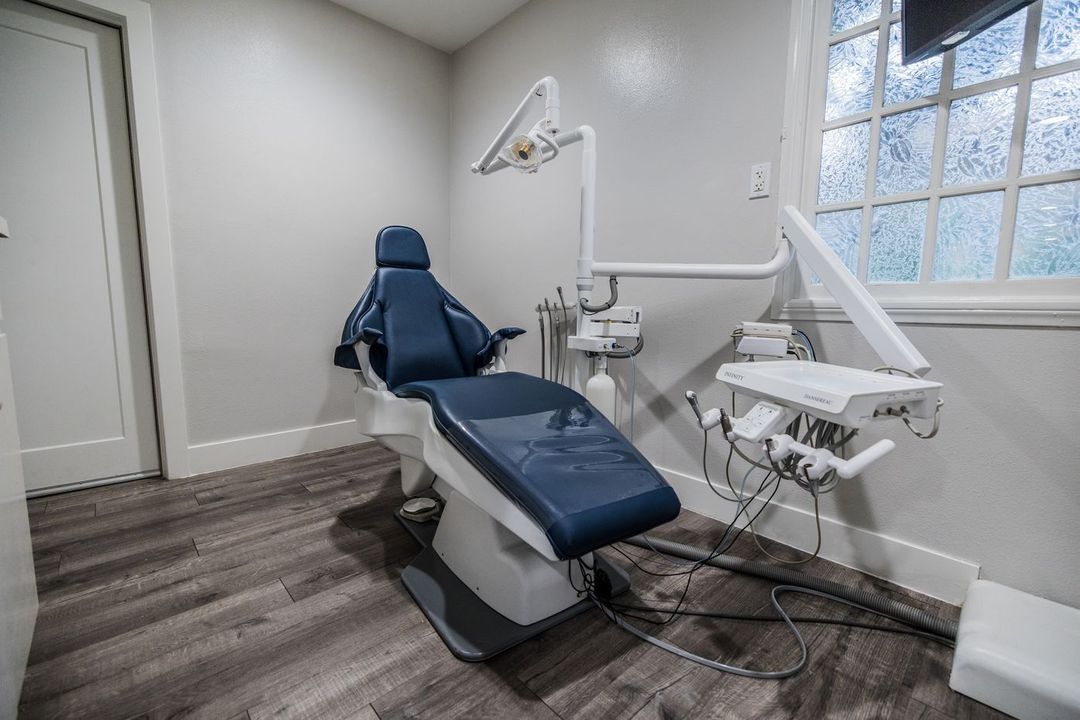 Dental chair in a light gray room, next to a window and medical equipment.