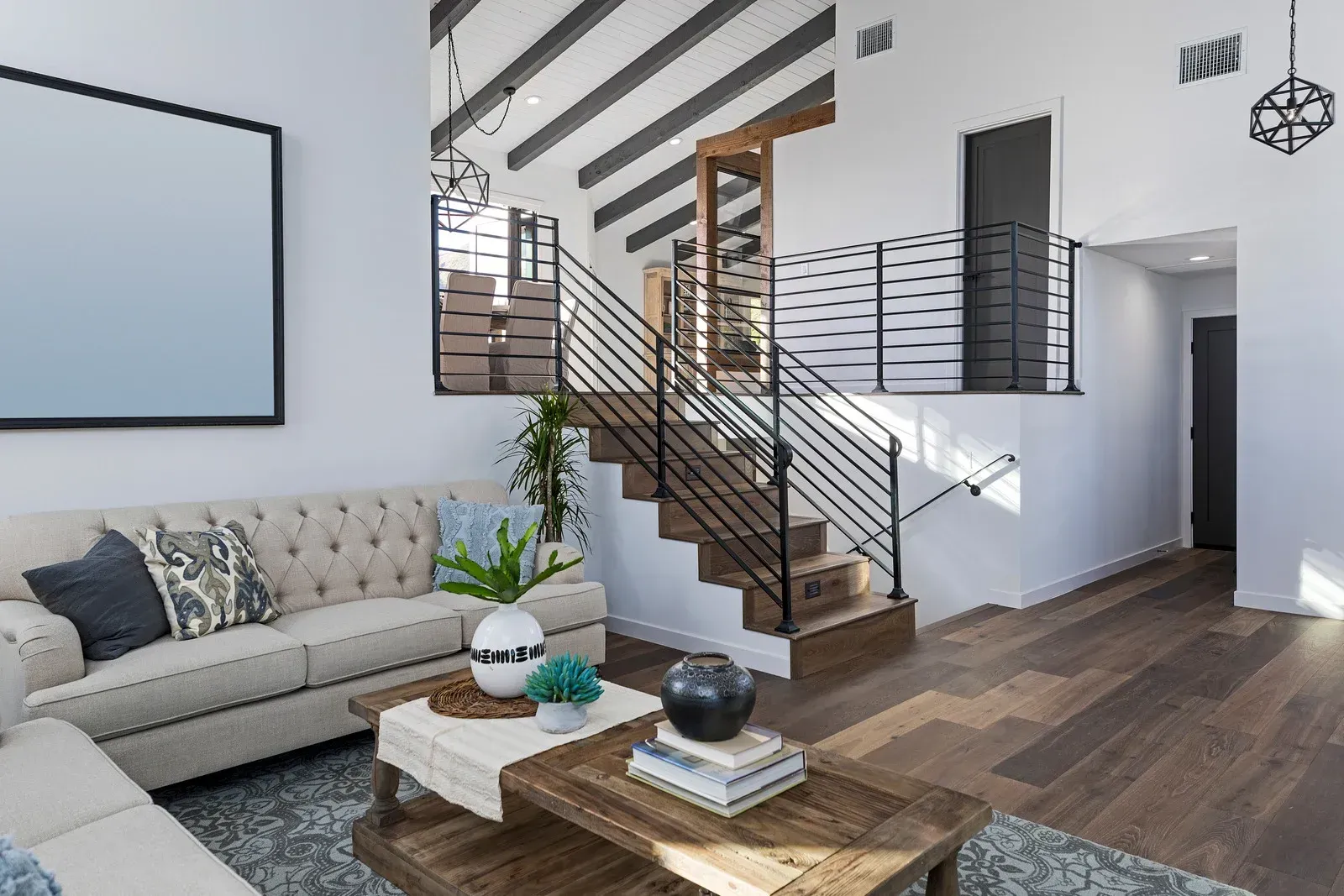 Living room with staircase, modern design. Light-colored sofa, wooden floors, black staircase railing.