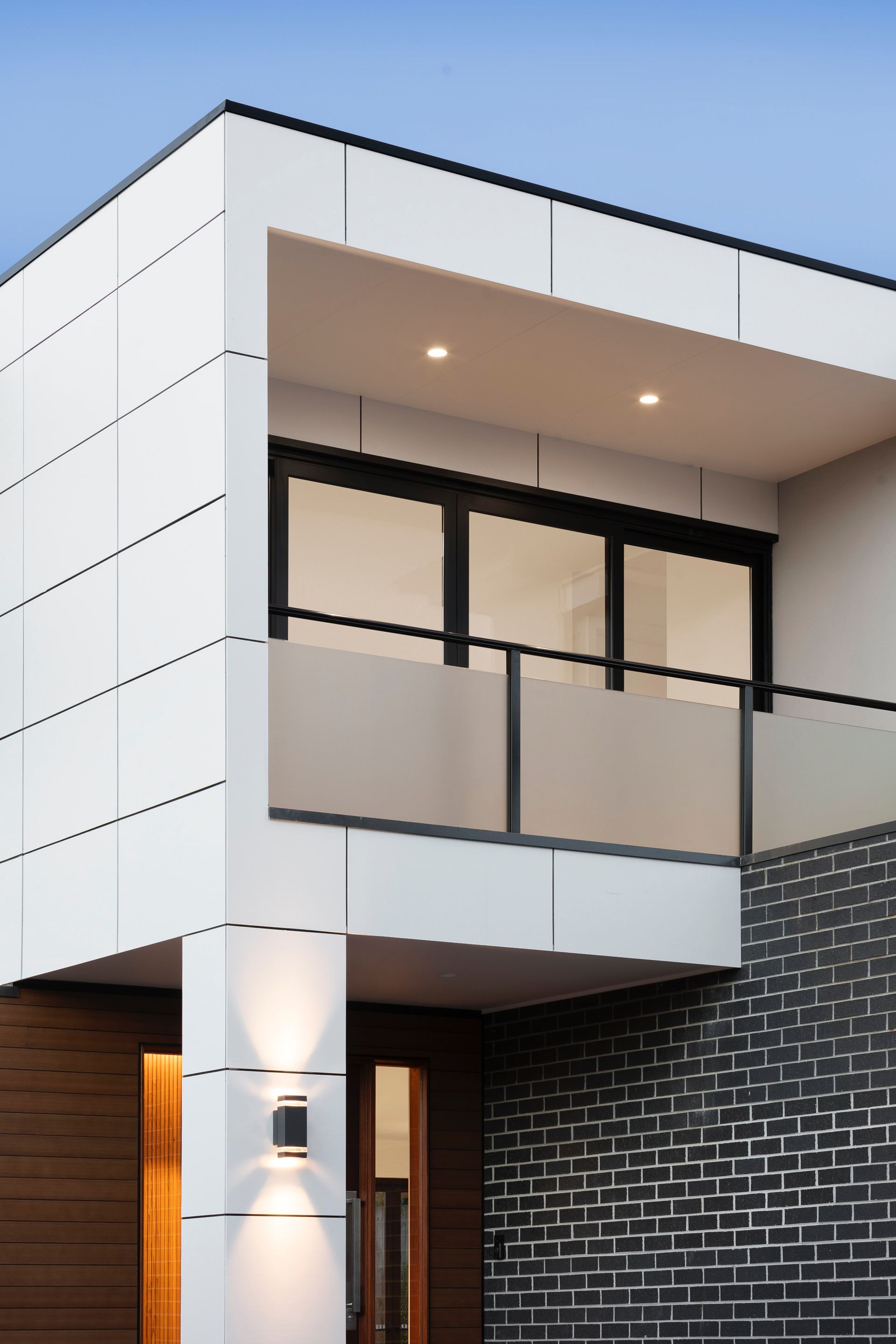 Modern two-story house exterior with white panels, large balcony, and dark brick accent wall