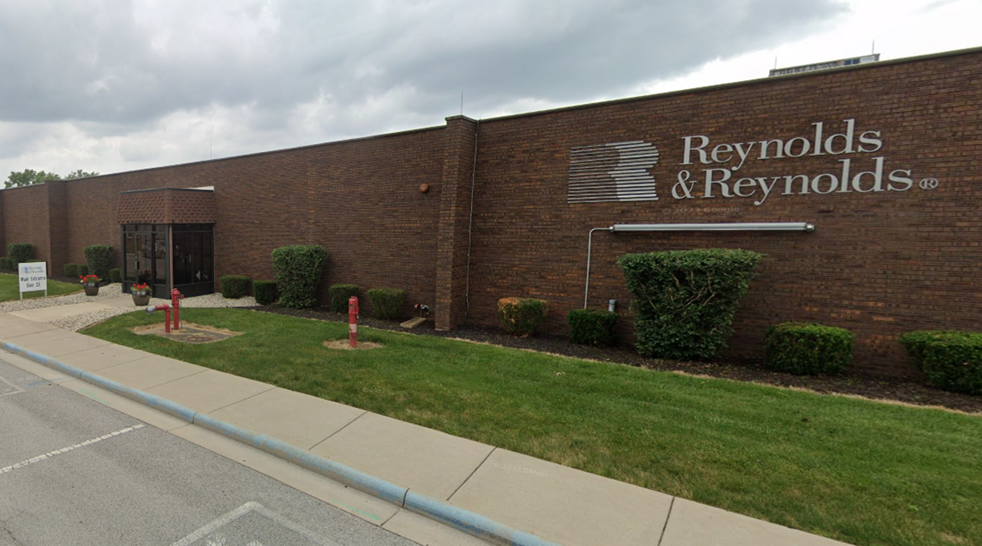 Reynolds & Reynolds building with logo on brick wall, green lawn, and overcast sky.