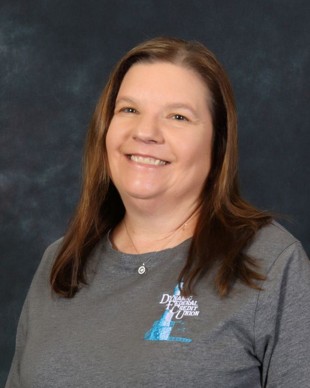 Woman in gray collared shirt, smiling, against blue backdrop.