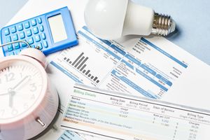 Pink alarm clock, calculator, lightbulb, and utility bill, representing energy costs and billing.