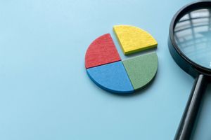 Pie chart in four colors with magnifying glass on a blue background.