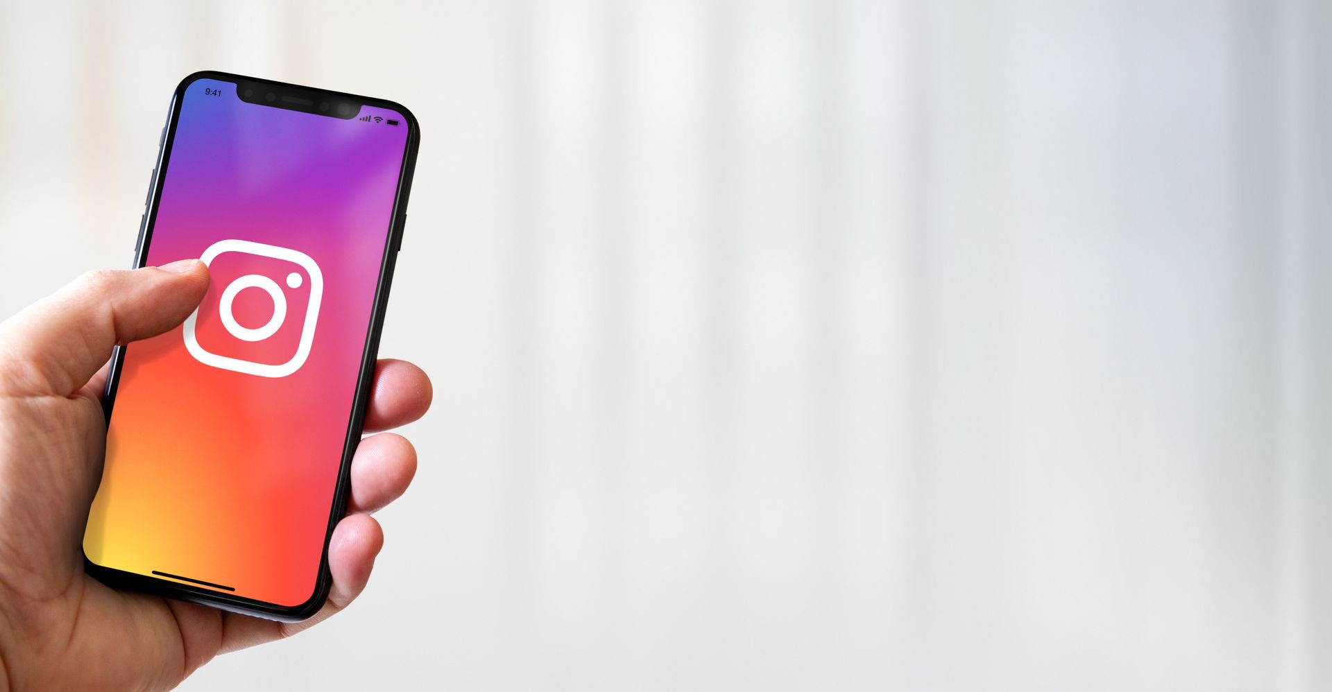 Hand holding a smartphone with the Instagram app logo on the screen.