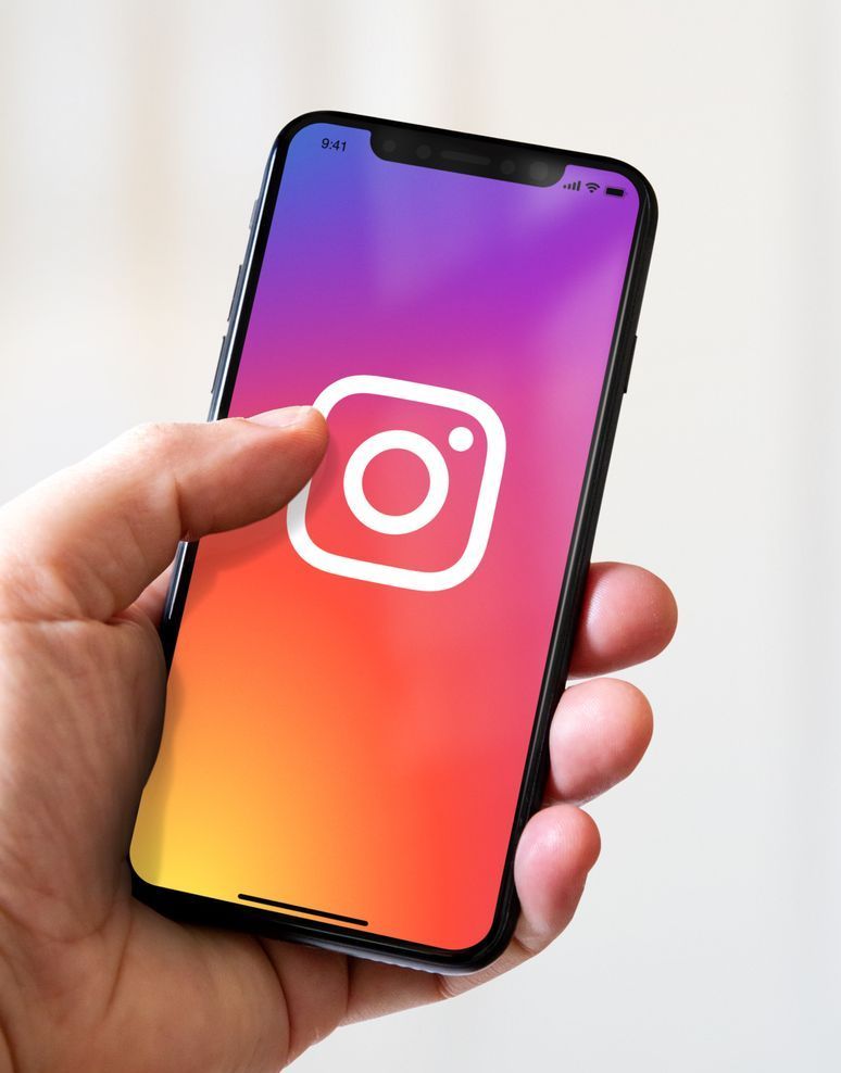 Hand holding a phone with the Instagram app logo displayed on the screen.