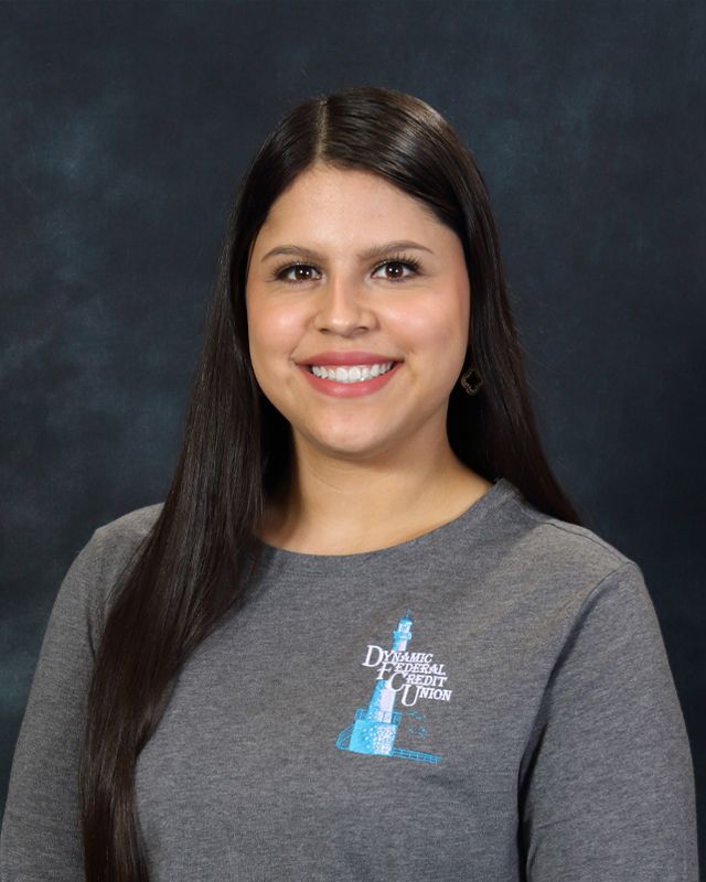 Woman with long brown hair, smiling, wearing a gray shirt, on a blue background.