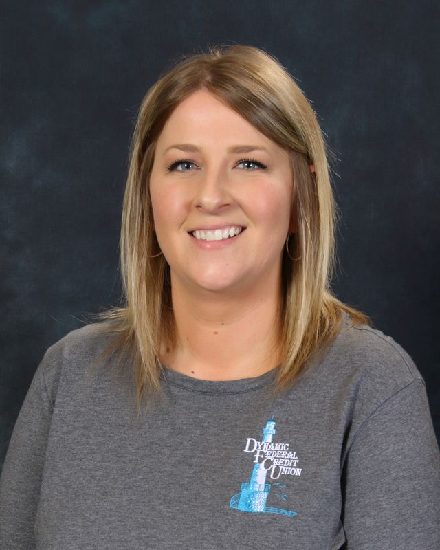 Woman with blonde hair wearing a gray collared shirt, smiling, blue background.