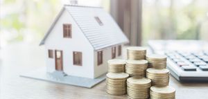 A miniature house next to stacks of coins and a calculator, symbolizing home finances.