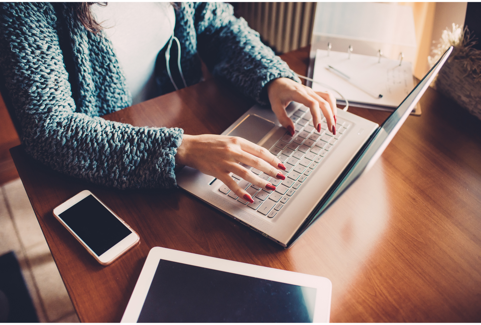 Picture of a home office remote laptop with a lady typing in her home office with a I pad and a Iphone sitting on the desk