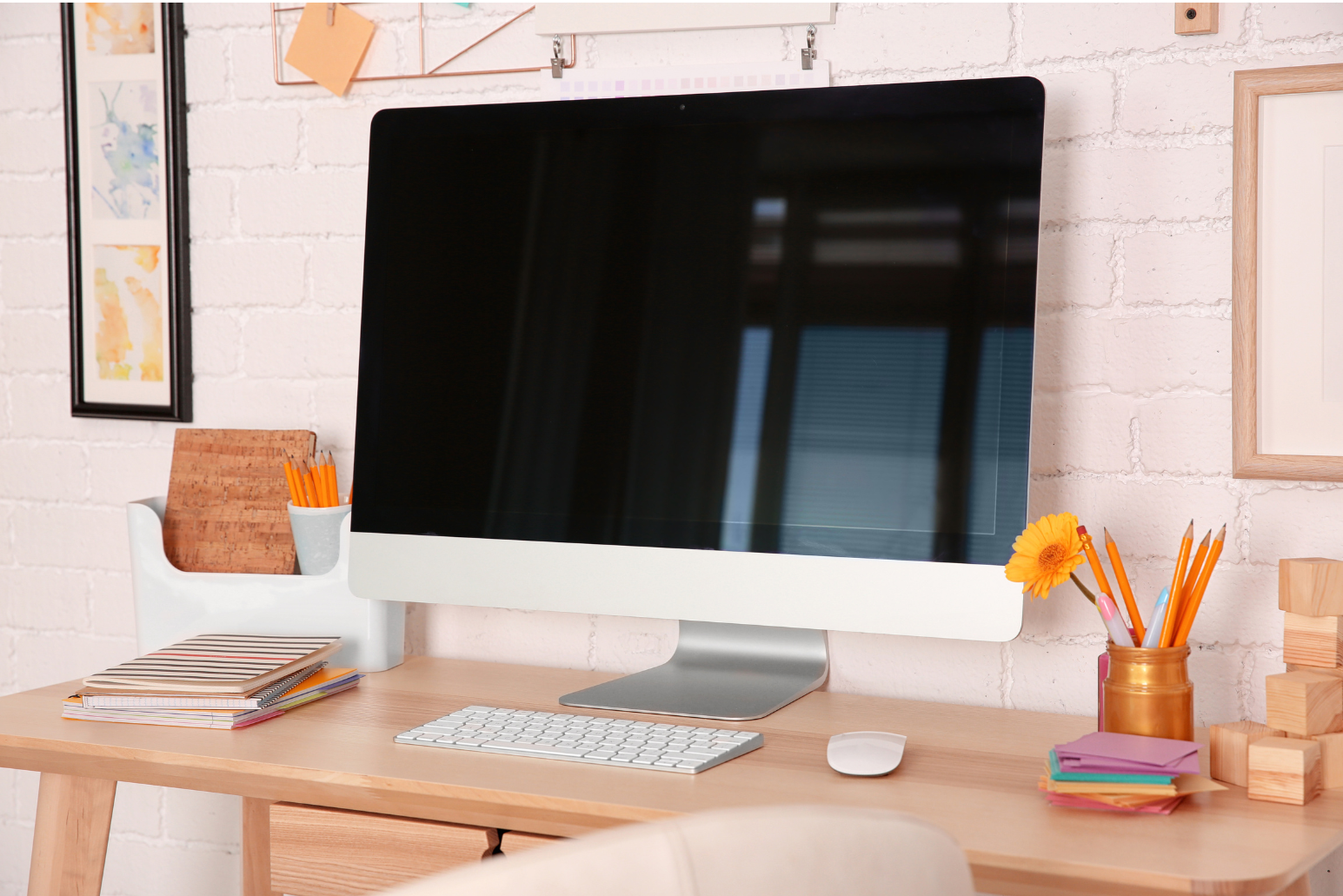 Picture of a Apple computer screen monitor with a wireless keyboard sitting on a wood work desk